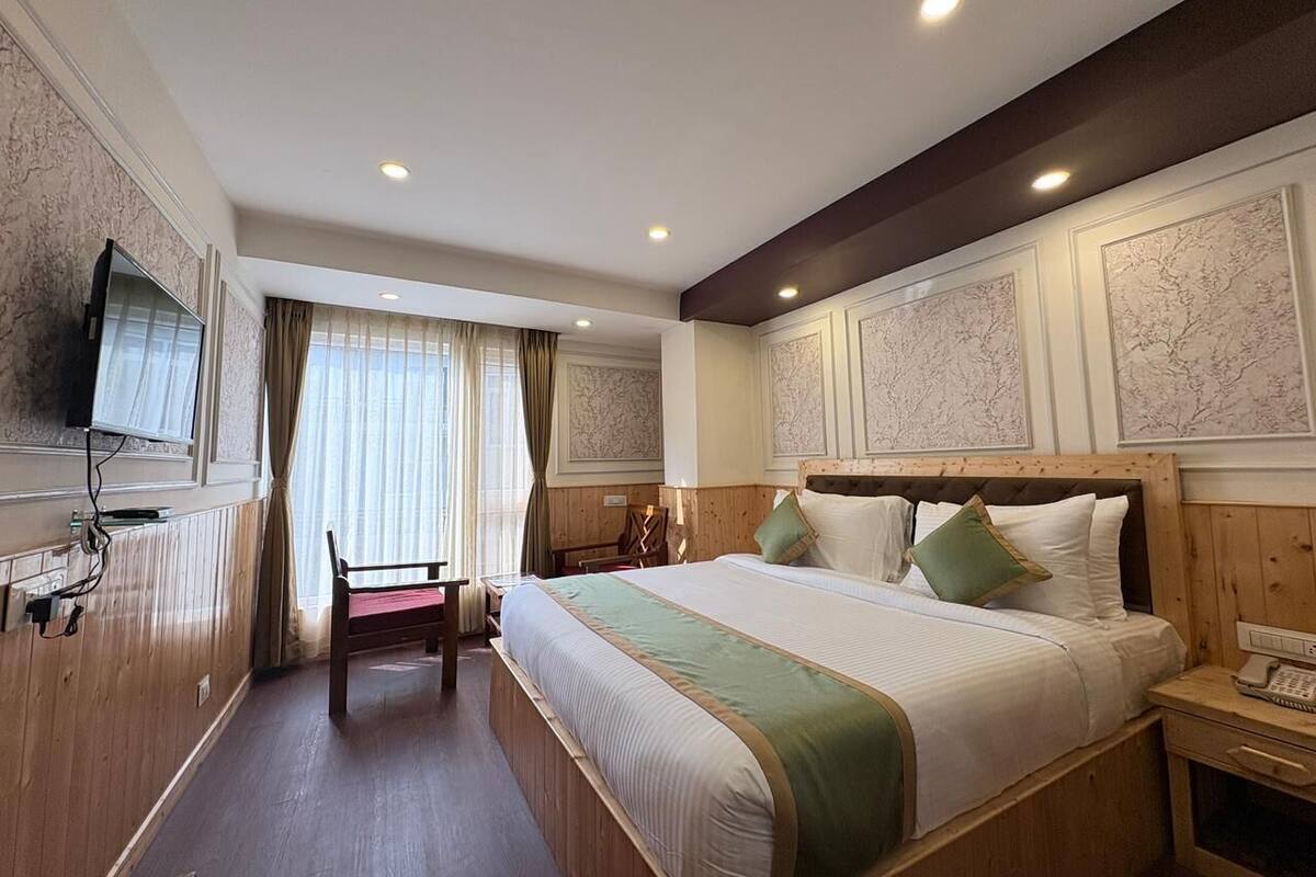 A hotel room with a large bed, a desk, a chair, and a television on the wall.