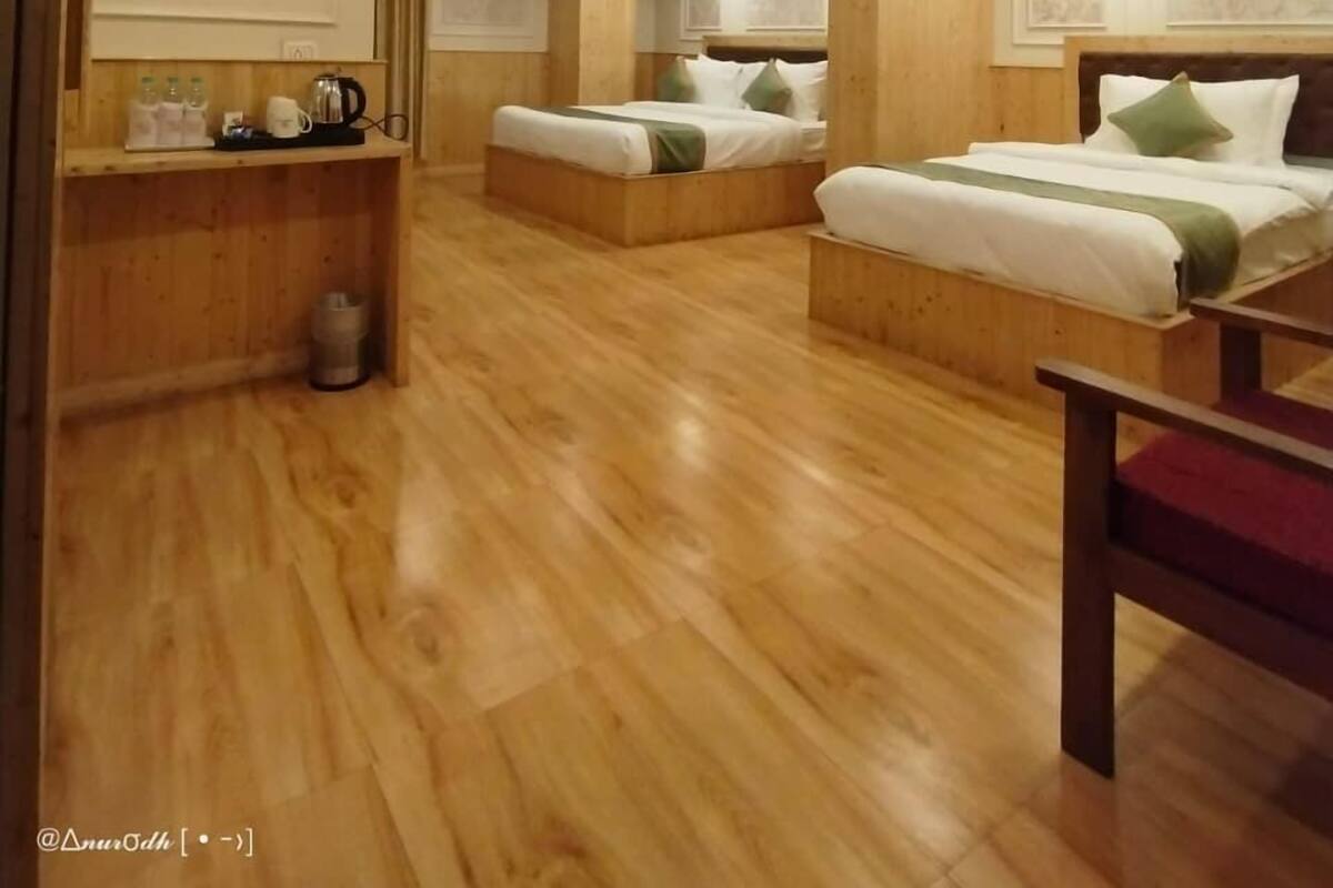 A hotel room with two beds, wooden flooring, a small desk with a kettle, and a trash bin.