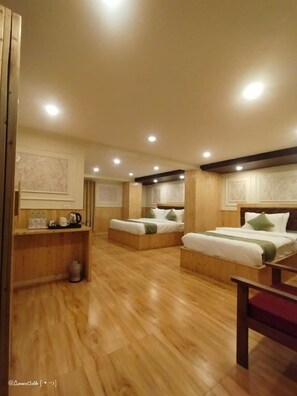 A hotel room with two beds, wooden flooring, a small desk with a kettle, and a trash bin. - WORMWOOD SYNERGY NEW MANDALA  (Darjeeling)
