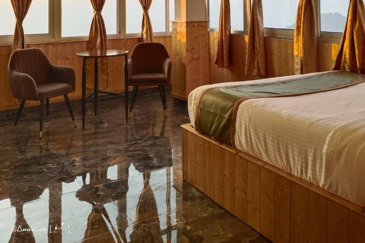 A room with a bed, two chairs, a small table, and large windows with curtains.