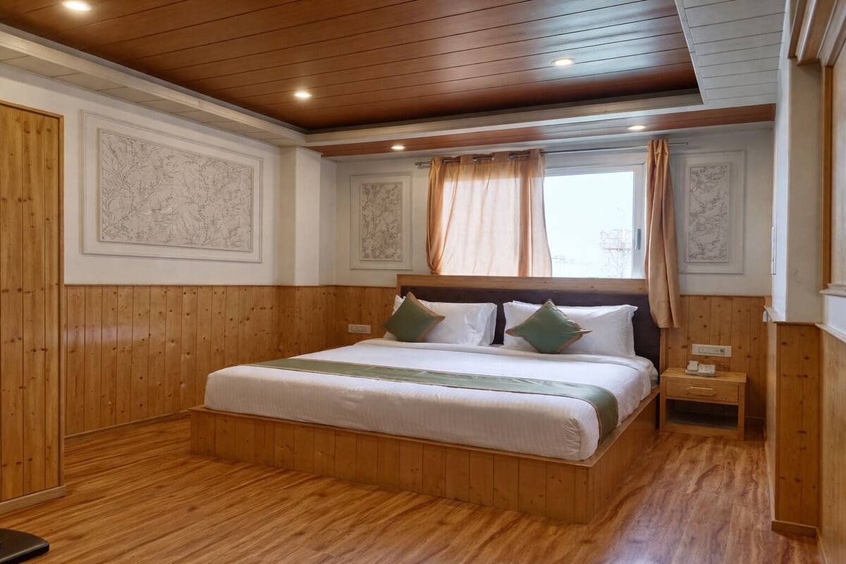 A wooden-paneled room with a large bed, two bedside tables, and a window with curtains.