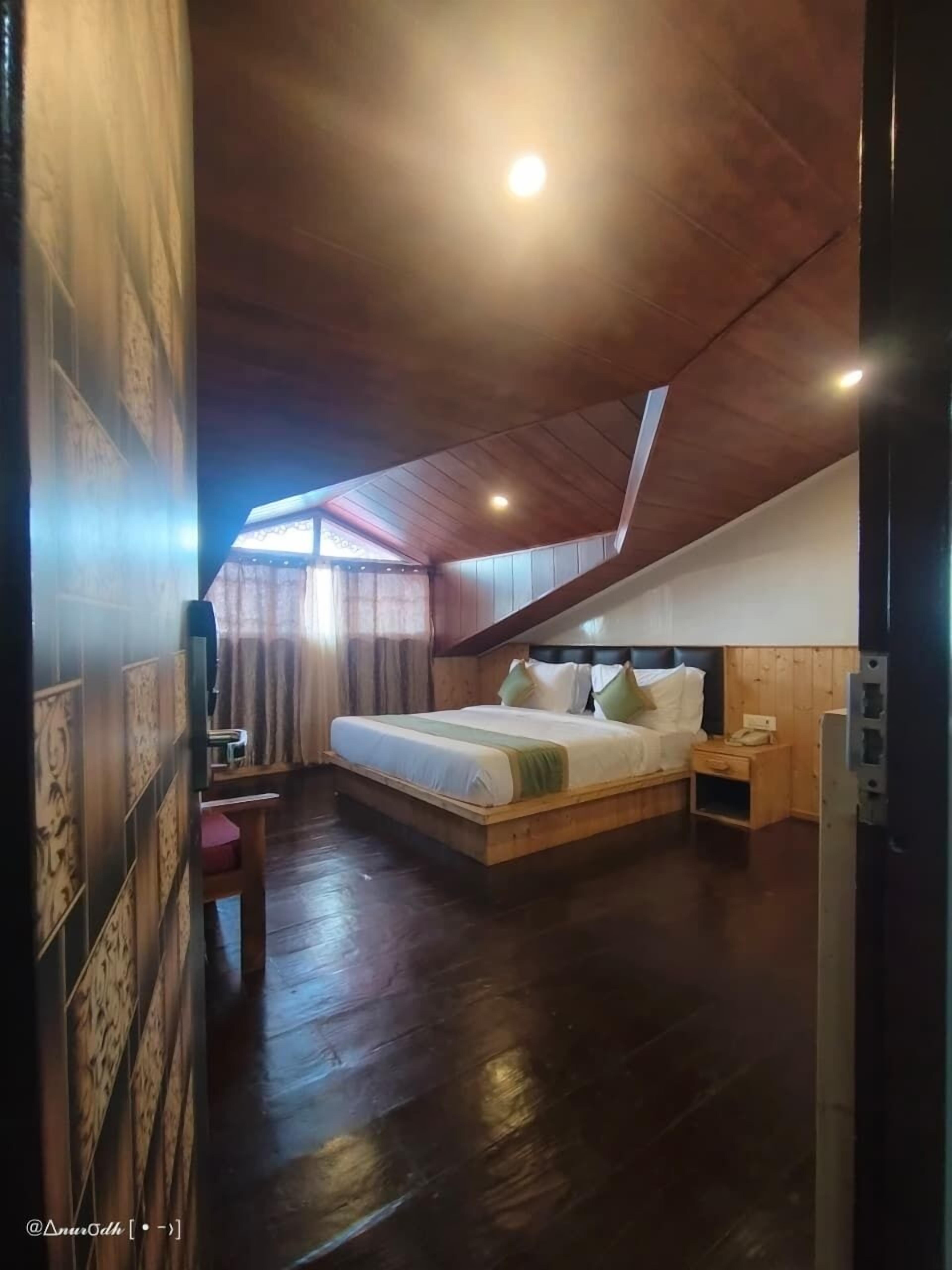 A bedroom with a wooden ceiling, a bed with pillows, a nightstand, and a window with curtains.