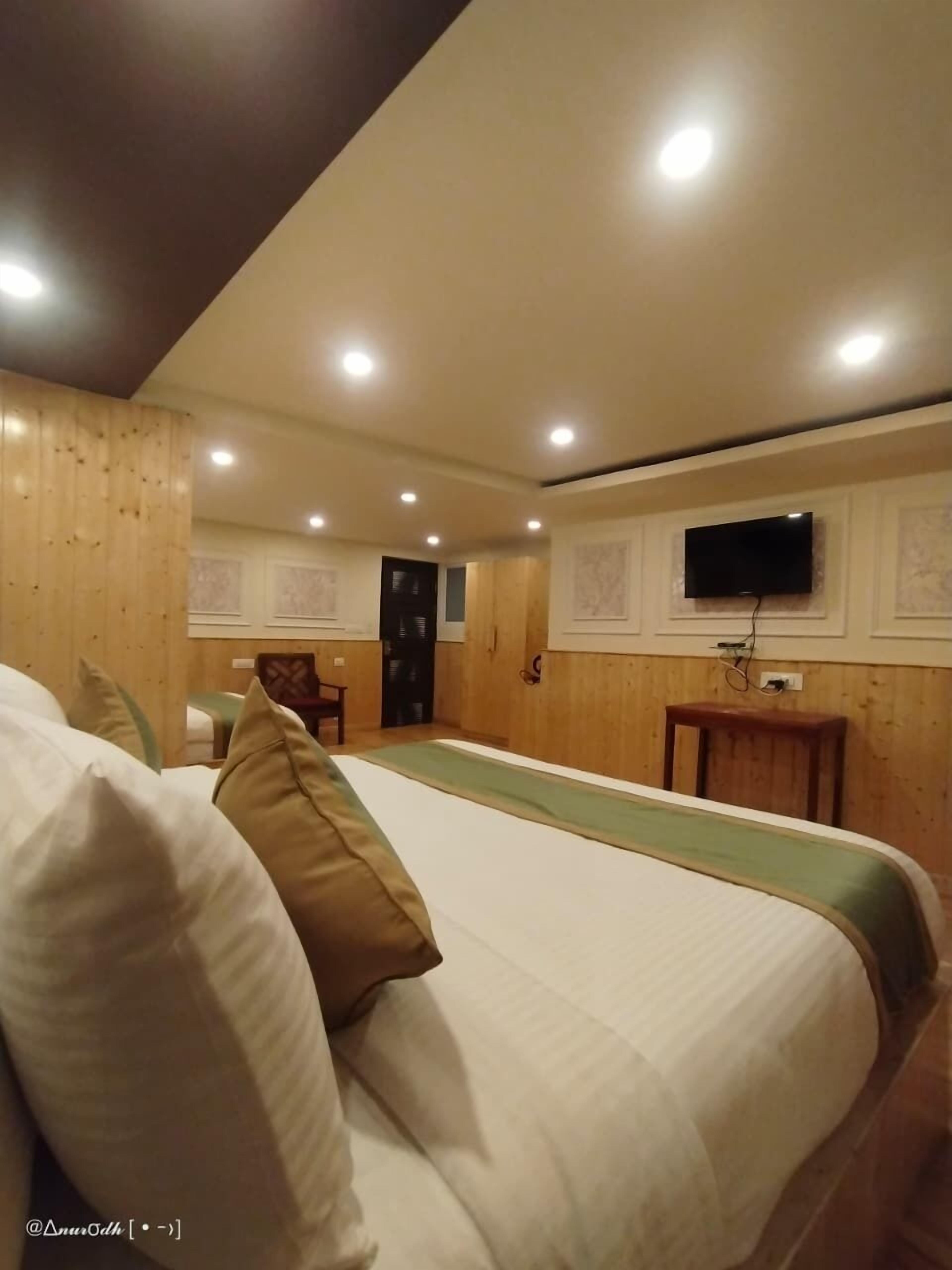 A hotel room with a large bed, wooden paneling, a television, and a small table.