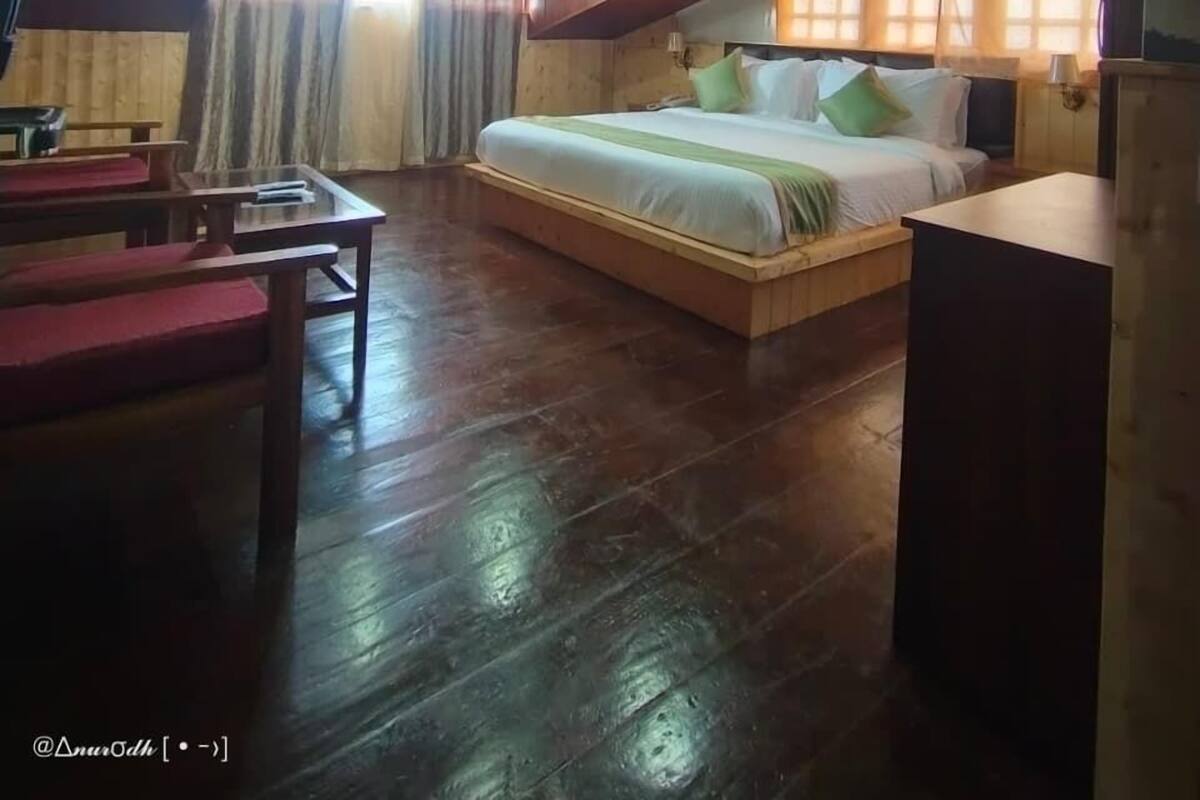 A bedroom with a sloped ceiling, wooden flooring, a bed with pillows, a bedside table, and a window with curtains.
