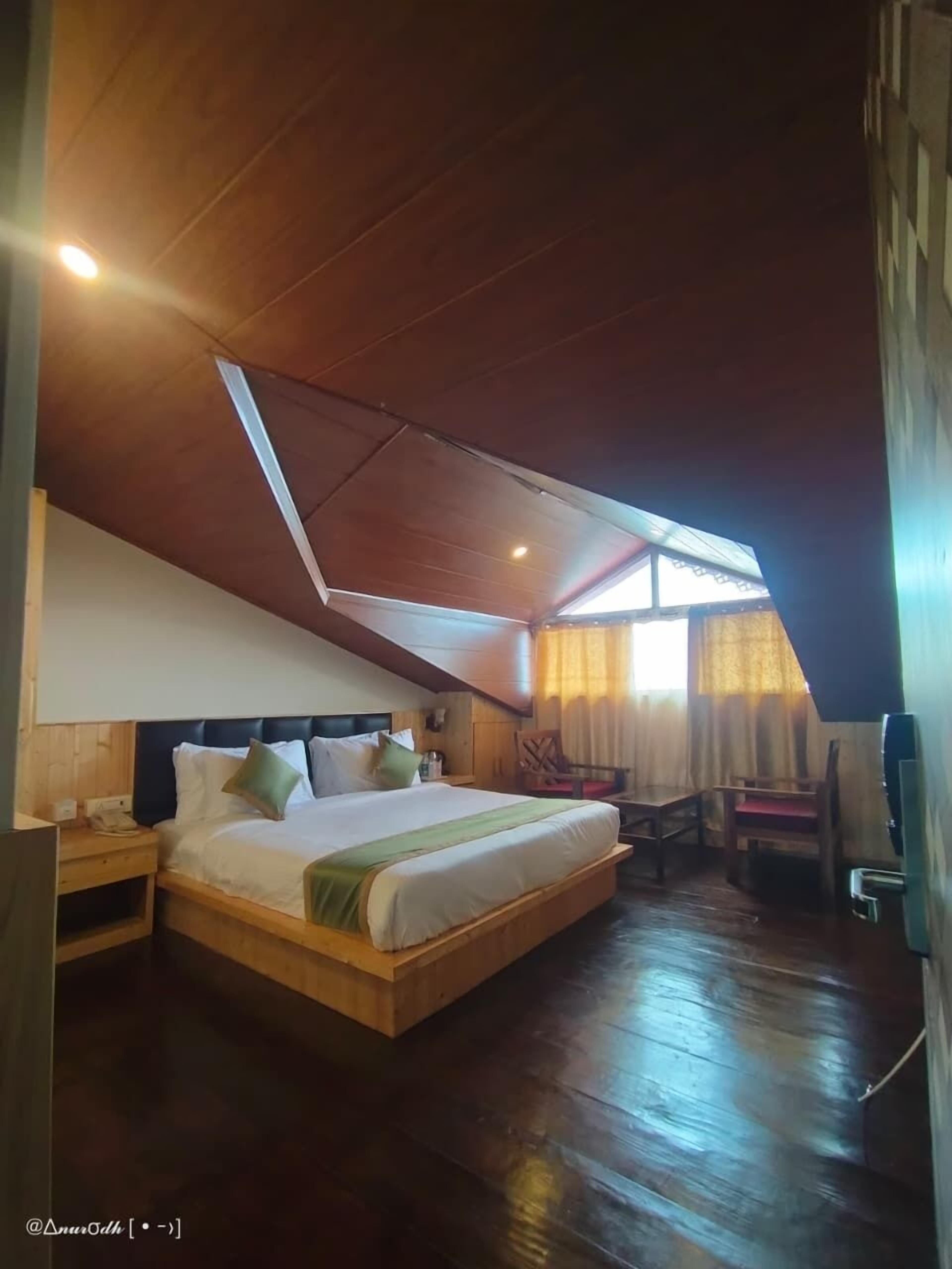 A bedroom with a sloped ceiling, a bed with pillows, a nightstand, a chair, and a desk.