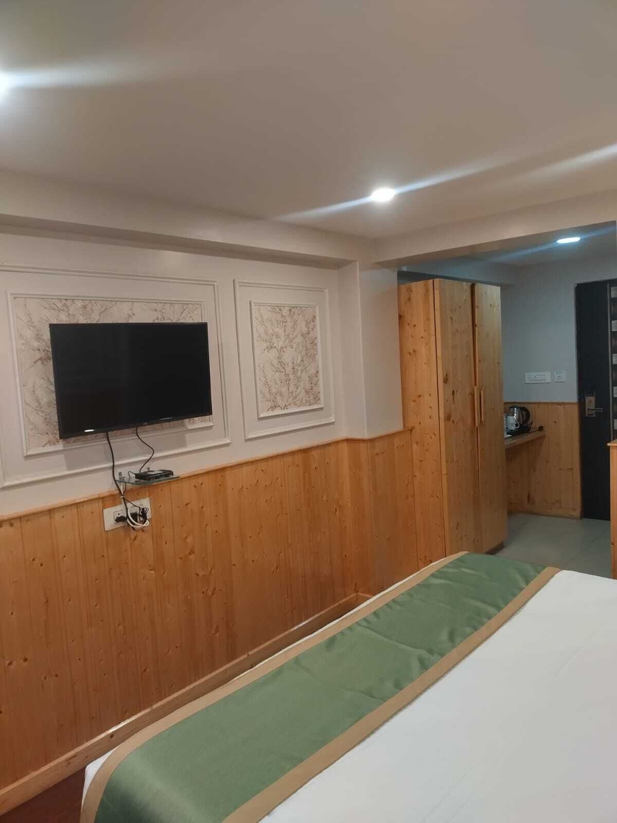 A room with a bed, a television mounted on the wall, wooden paneling, and a door leading to another room.