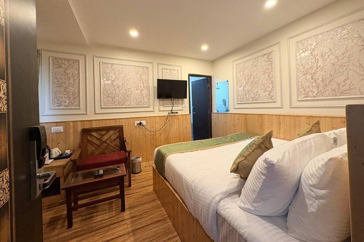 A hotel room with a bed, a chair, a desk with a coffee machine, and a television on the wall.