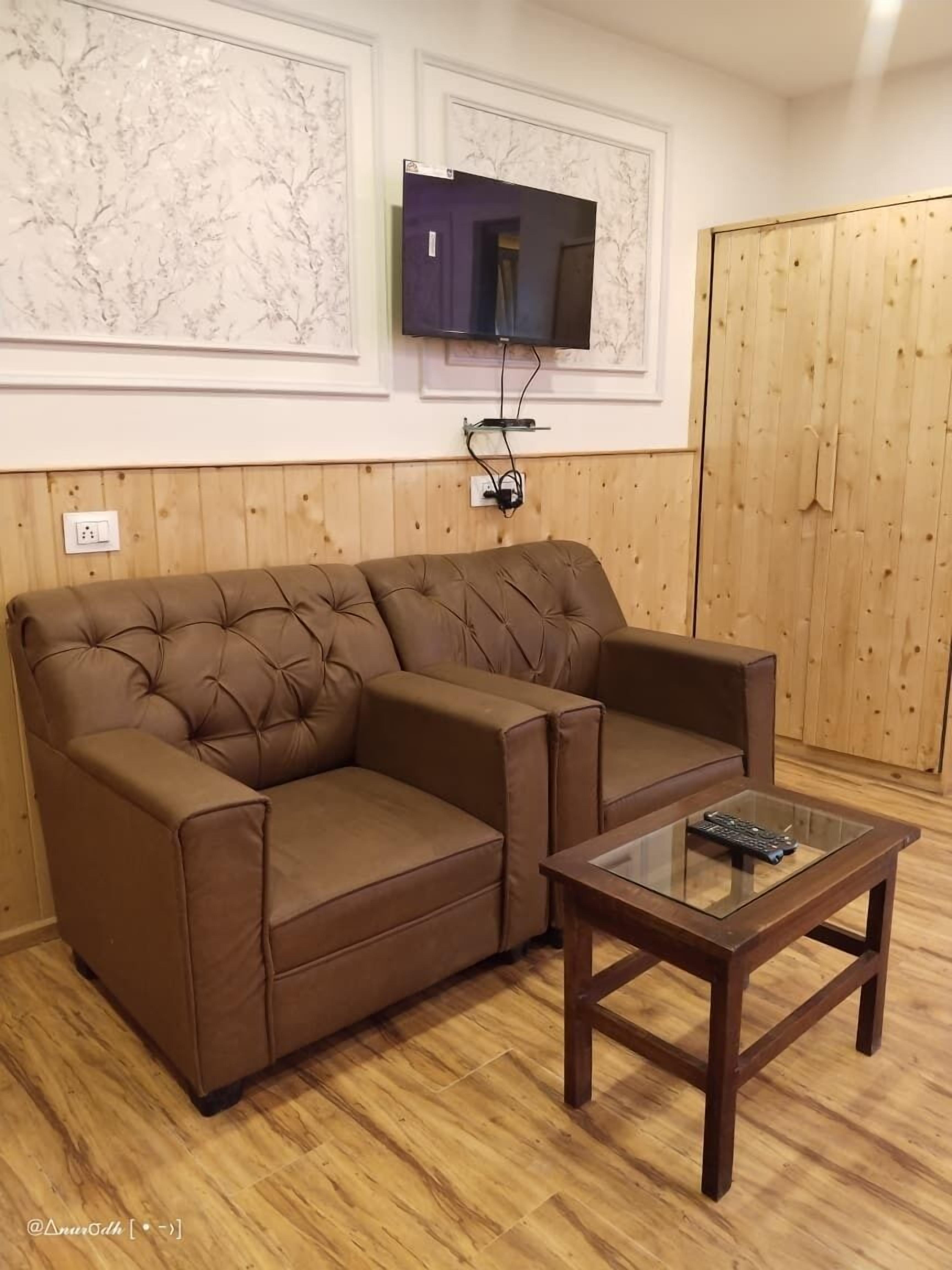 Un sofá seccional marrón con una mesa de centro de vidrio en una habitación con paredes de madera y un televisor montado.