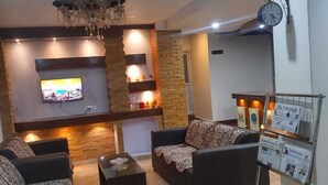 A modern living room with a fireplace, sofas, a coffee table, and a TV. - WORMWOOD SYNERGY NEW MANDALA  (Darjeeling)