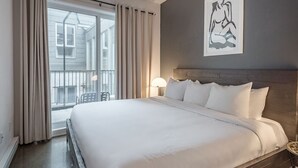 Une chambre d’hôtel avec un grand lit, une vue sur l’extérieur, une œuvre d’art accrochée au mur et une table de chevet avec une lampe.