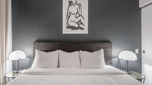 Une chambre à coucher avec un lit, deux tables de chevet avec des lampes, une tête de lit en bois foncé et une œuvre d’art encadrée accrochée au mur.