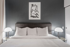 A bedroom with a bed, two bedside tables with lamps, a dark wooden headboard, and a framed artwork on the wall. - Luxury Old Montreal Suite with Soaring Ceilings (Montréal)