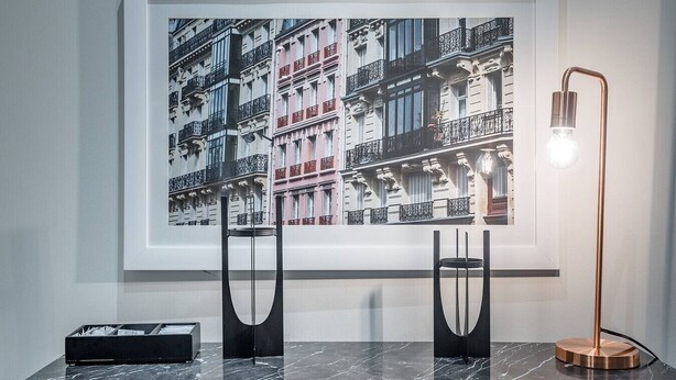 Une photographie encadrée représentant un bâtiment doté de balcons, une lampe de sol moderne et une boîte de rangement noire posée sur une surface en marbre.