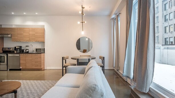 A modern living room with a sofa, a dining table, and a kitchen area with wooden cabinets and appliances. - Chic Old Montreal Apt with Terrace (Montréal)