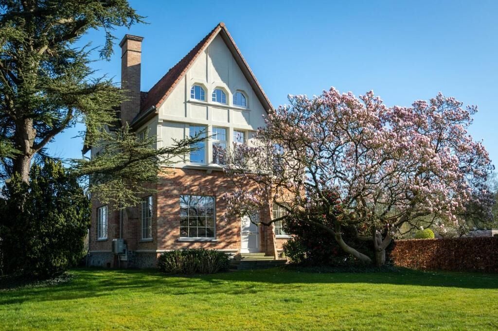 A two-story house with a brick facade, large windows, and a chimney.