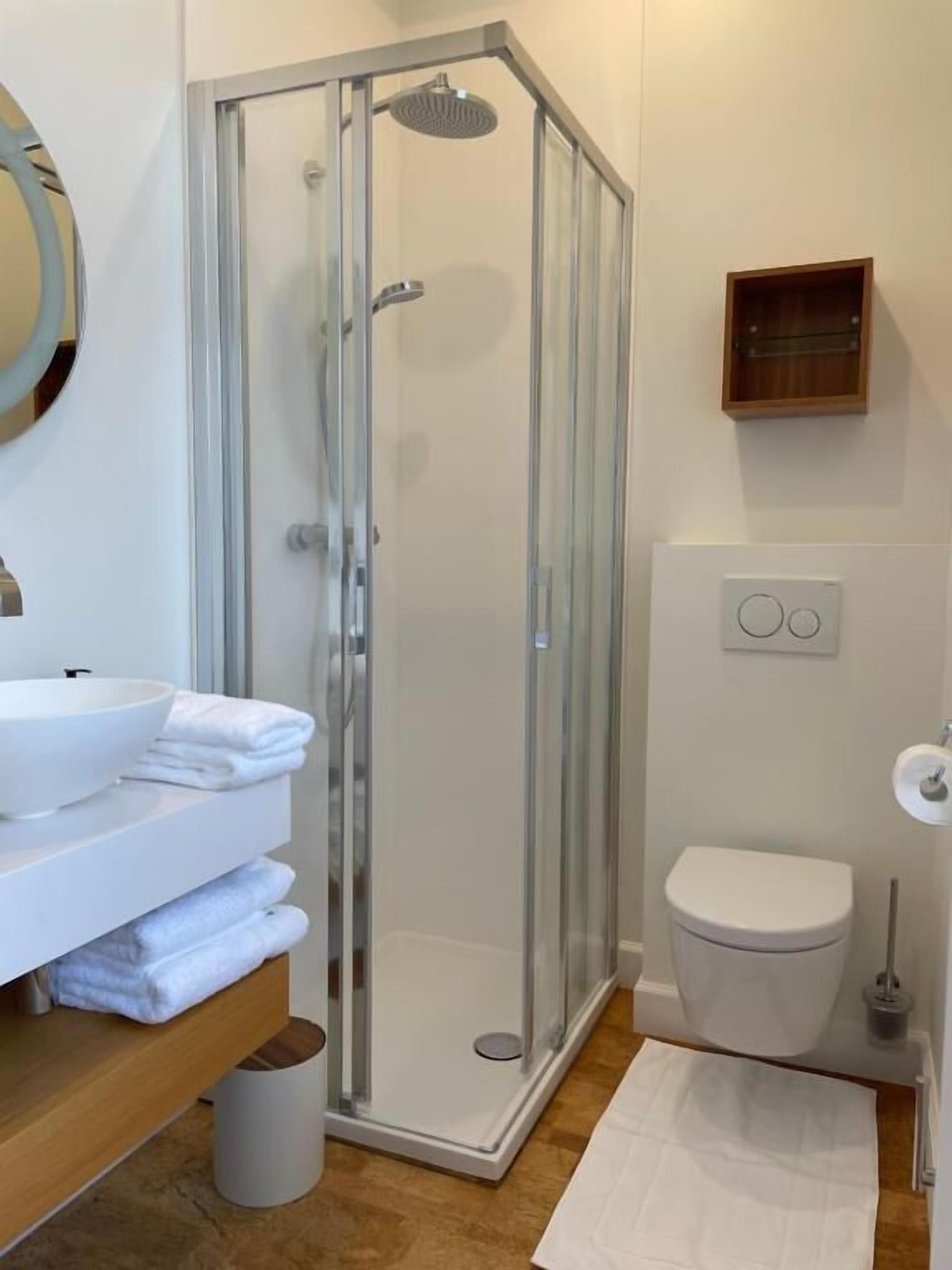 Ein modernes Badezimmer mit einer Glaskabine zur Dusche, einem weißen Waschbecken mit Schüssel und einer Toilette.