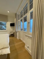 Un dormitorio con cama, una silla, un escritorio, un televisor y una ventana con cortinas.