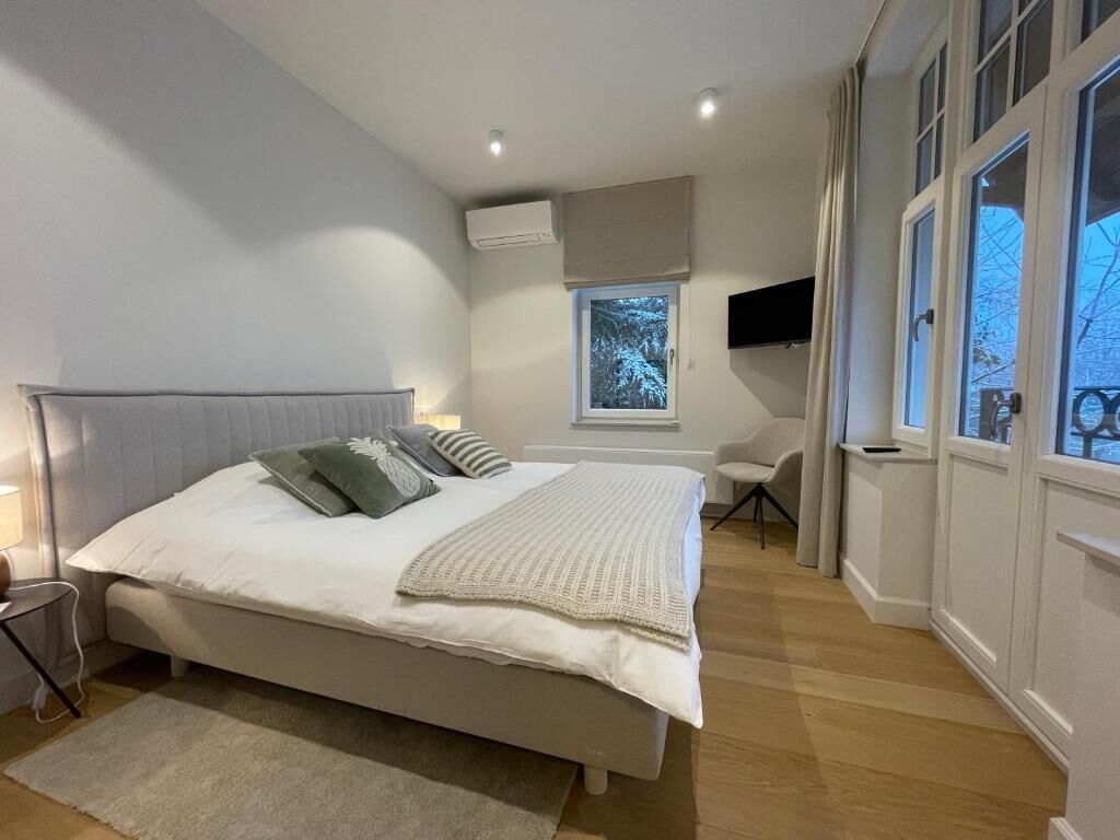 A bedroom with a large bed, a window, a TV, and a chair.