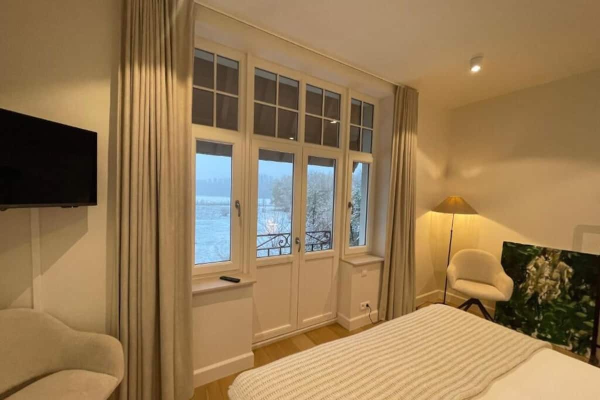 A hotel room with a bed, a chair, a TV, a window with curtains, and a painting.