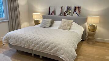A bedroom with a large bed, two bedside lamps, and abstract art on the wall.