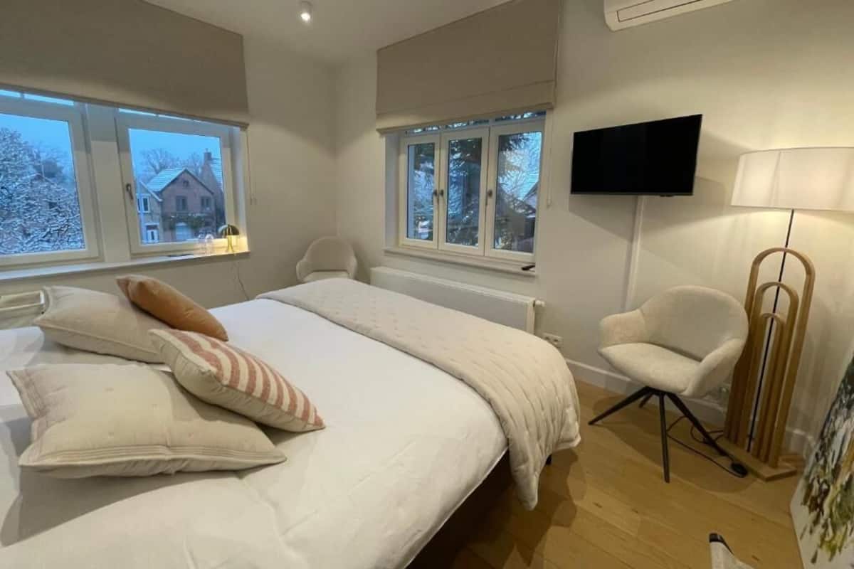 A bedroom with a bed, a chair, a TV, and a window.