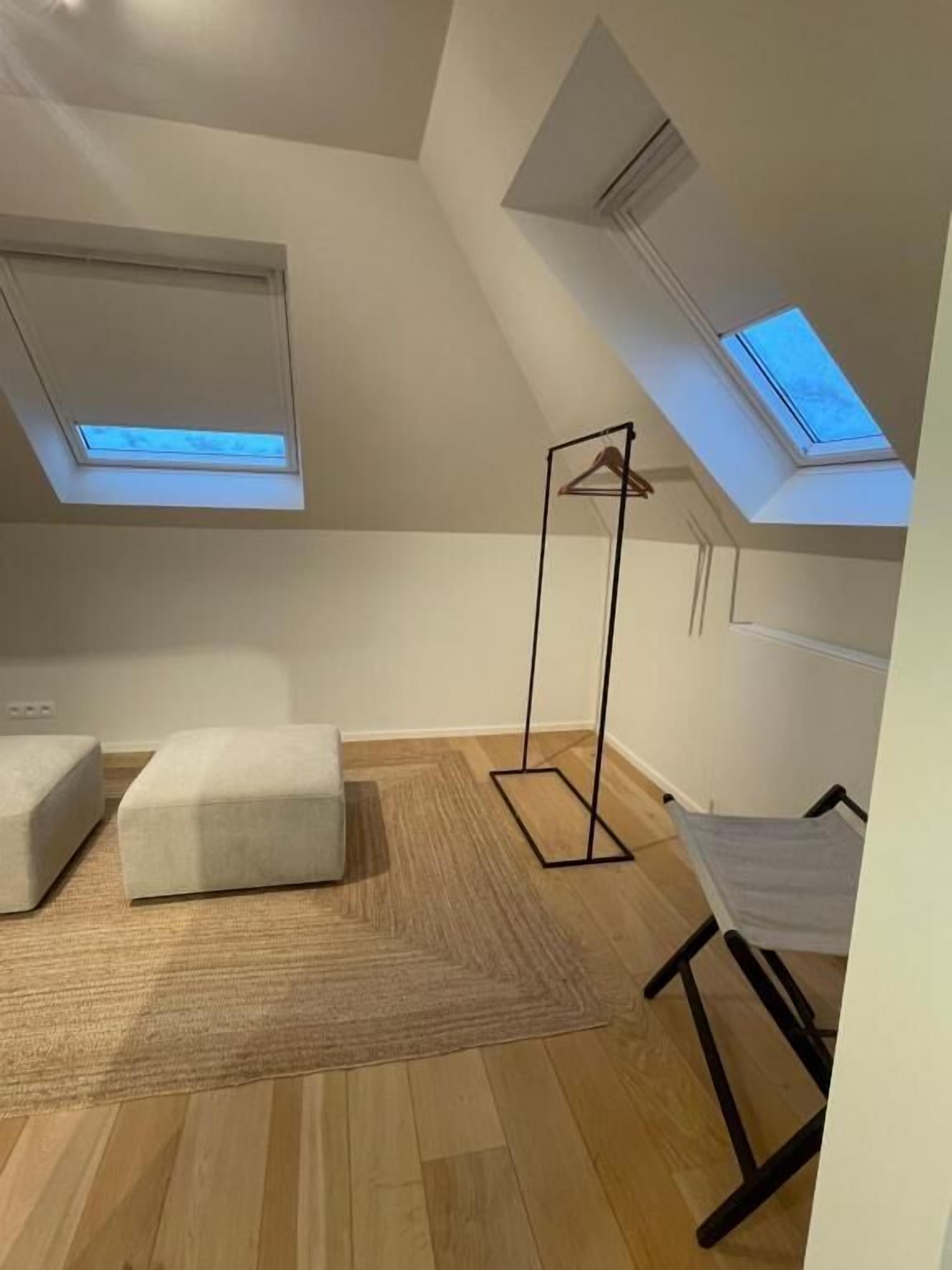 A modern loft bedroom with skylights, a hanging chair, and a large window.
