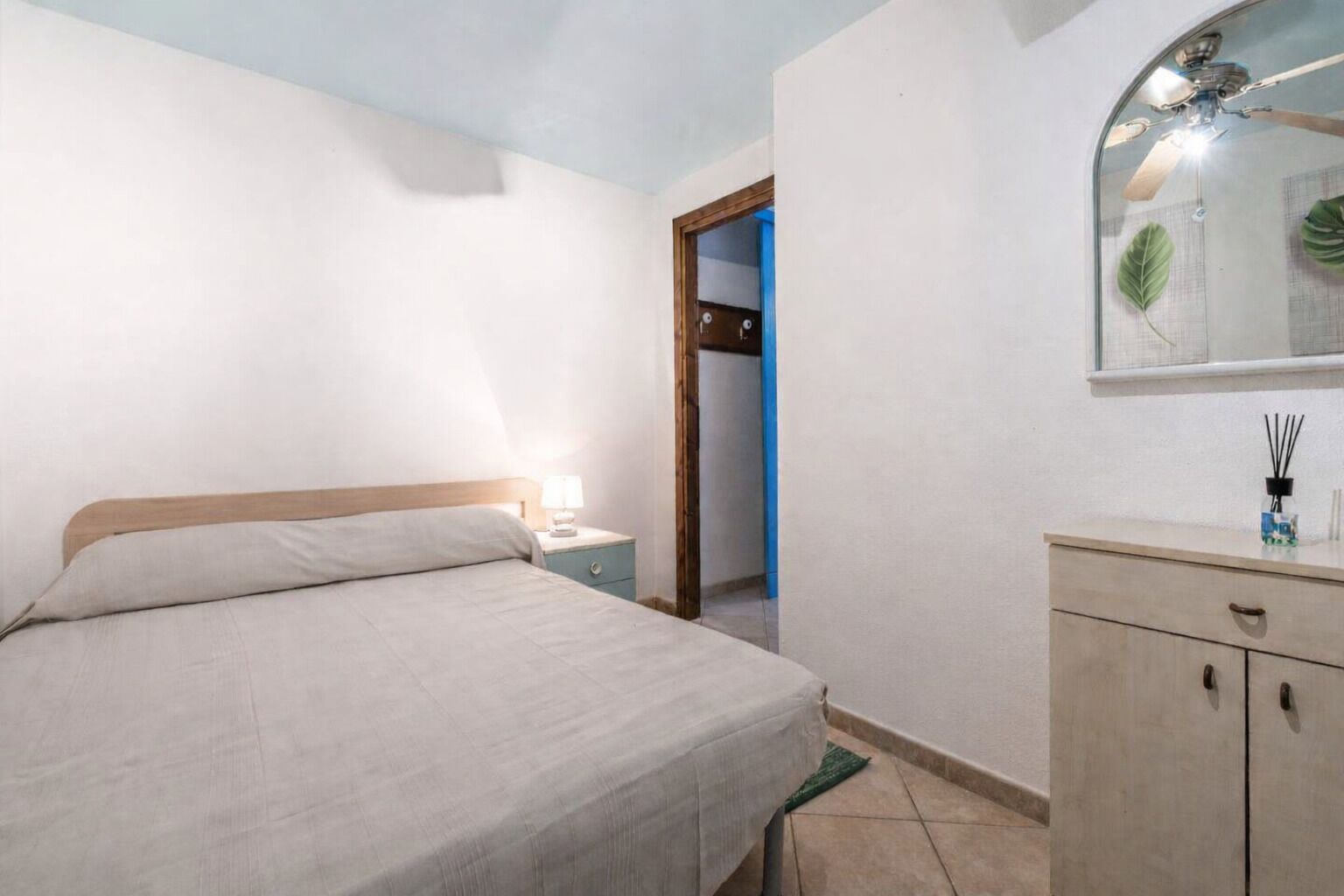 A bedroom with a bed, nightstand, dresser, and a mirror.