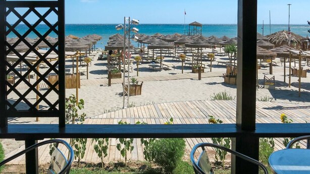 Vista sulla spiaggia da un'area ombreggiata con ombrelloni e lettini.