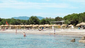 Una spiaggia con ombrelloni e lettini, cielo sereno e montagne sullo sfondo.