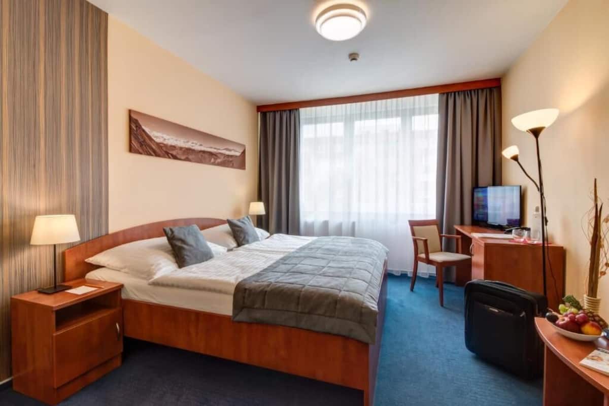 A hotel room with a large bed, a desk with a computer, a TV, and a small seating area.
