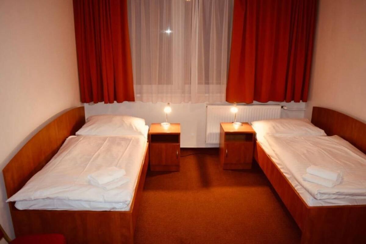 A hotel room with two single beds, each with a wooden headboard, white linens, and bedside lamps.