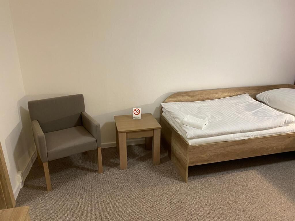 Ein Zimmer mit einem hölzernen Bett, einem grauen Sofa und einem kleinen Nachttisch mit einem Rauchverbot-Schild.