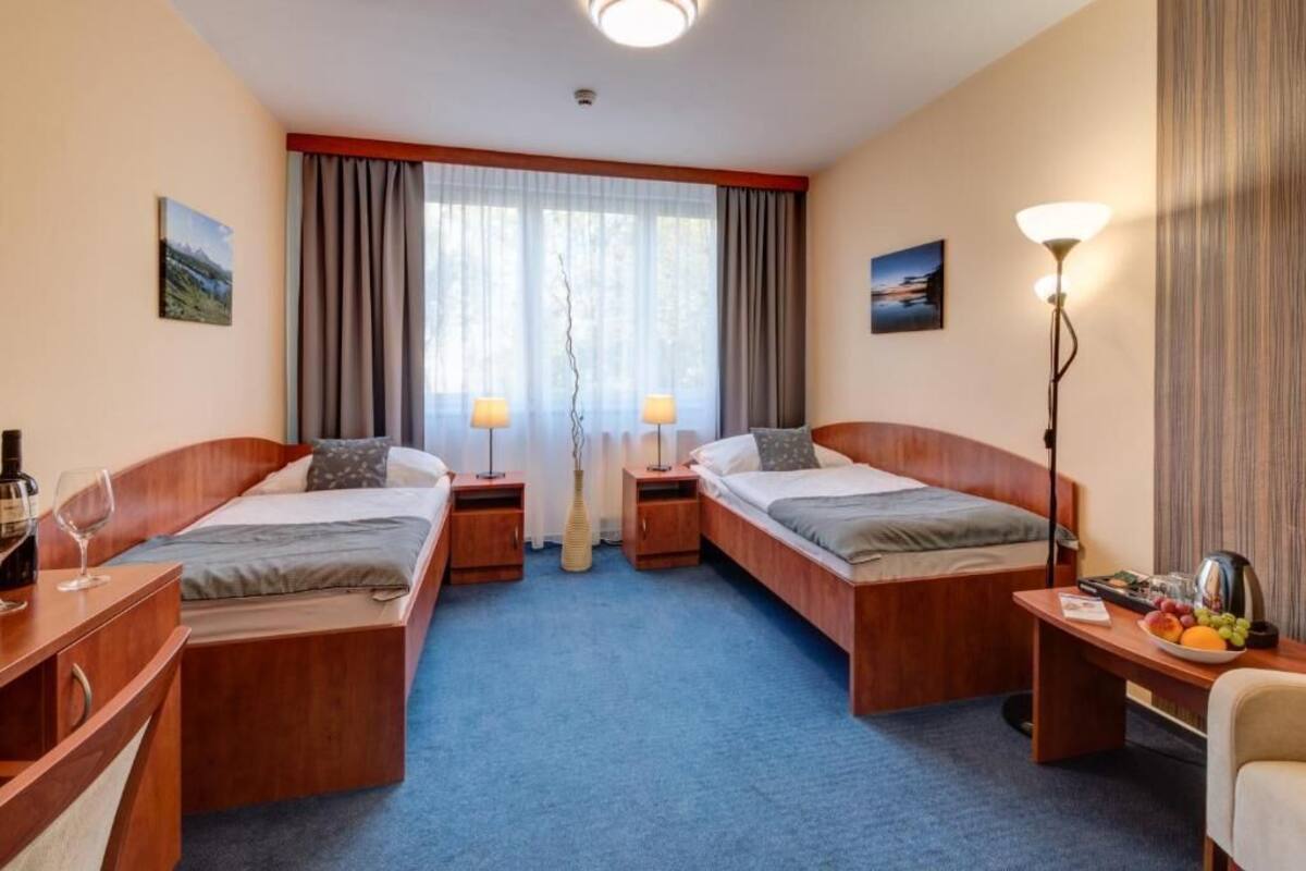 A hotel room with two single beds, a desk with a chair, a small table with a lamp, and a fruit bowl.