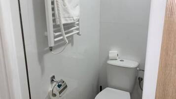 A small, clean bathroom with white tiles, a white toilet, a towel rack, and a toilet paper holder.