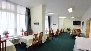 A dining area with multiple tables and chairs, large windows with sheer curtains, and a flat-screen TV mounted on the wall. - LC Hotel Ostrava (Ostrava)