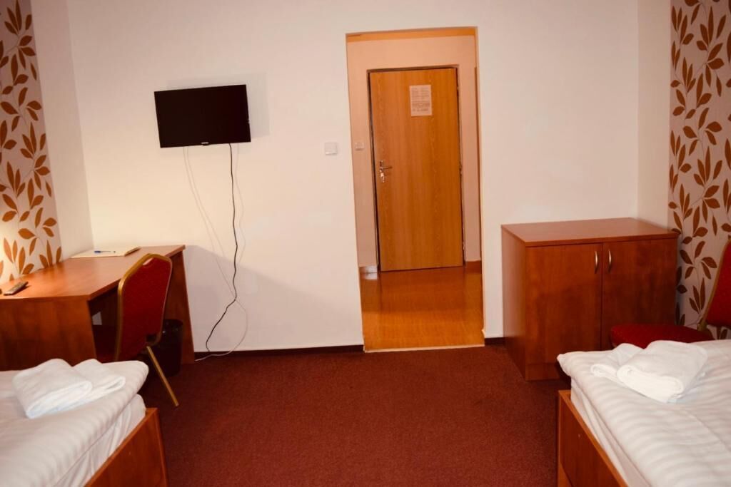 A hotel room with a bed, a desk, a chair, a TV mounted on the wall, and a wooden door.