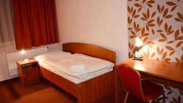 A hotel room with a wooden bed, a bedside table with a lamp, a red chair, and a wall with a leaf pattern.