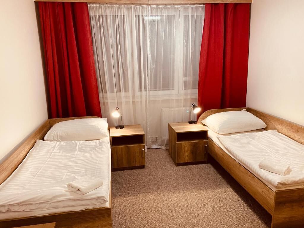 Una habitación pequeña y acogedora con dos camas de madera, cada una con una mesita de noche y una lámpara.