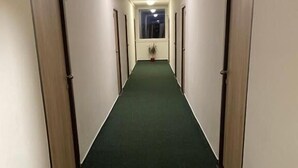A hallway with green carpet, wooden doors, and a window at the end. - LC Hotel Ostrava (Ostrava)