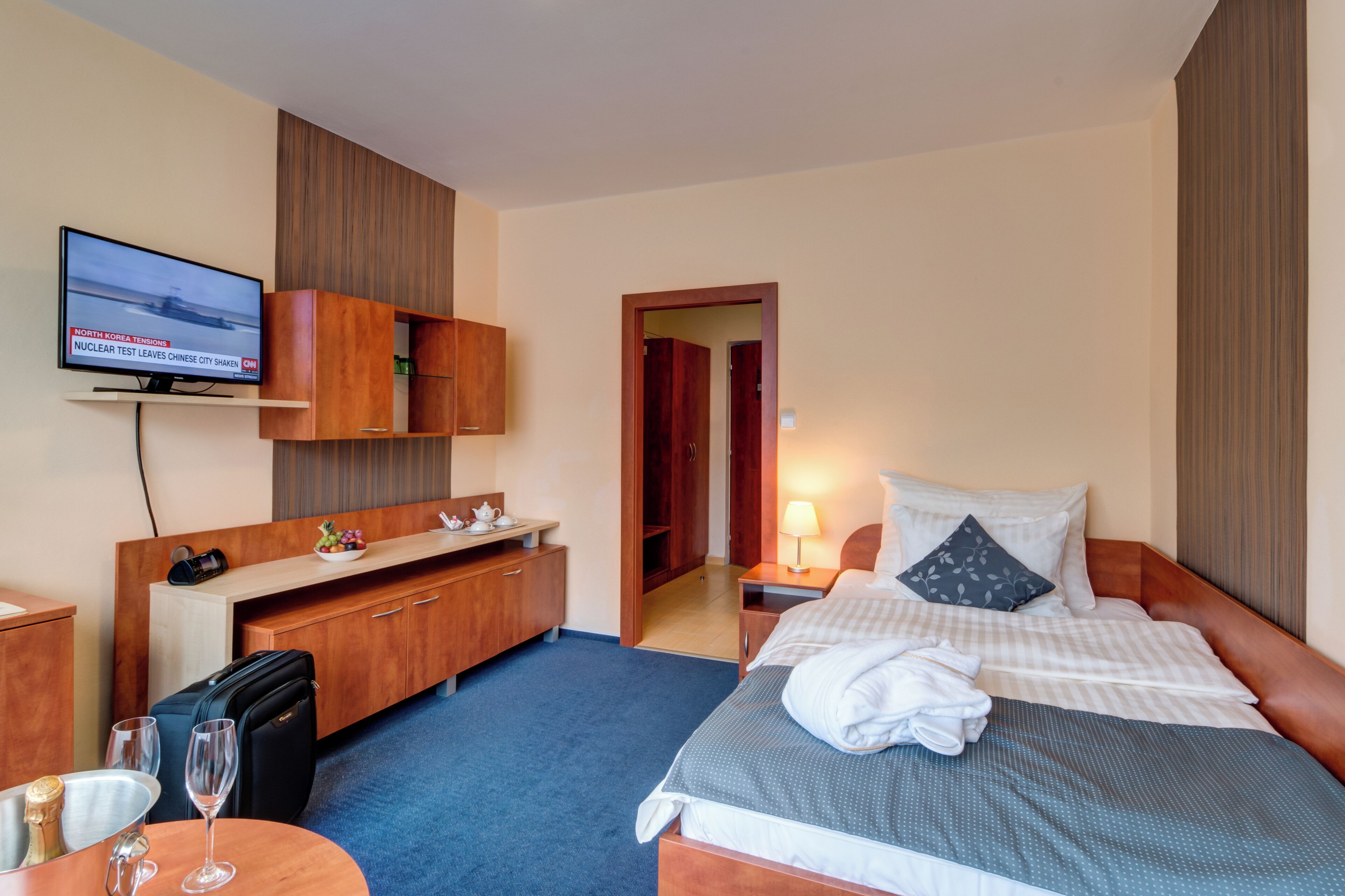 Ein Hotelzimmer mit einem Bett, einem Schreibtisch mit Computer, einem Fernseher und einem kleinen Tisch mit Glas und Flasche.