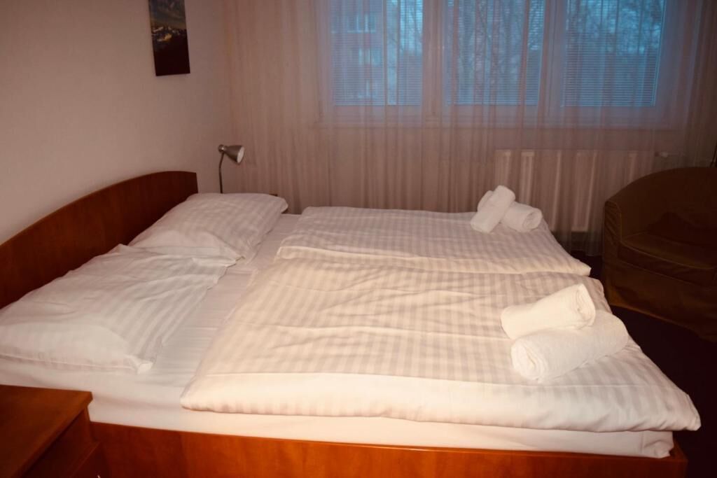 Ein ordentlich bezogenes Bett mit weißen Leinen und Handtüchern, ein Holz-Kopfteil und ein Fenster mit durchsichtigen Vorhängen.
