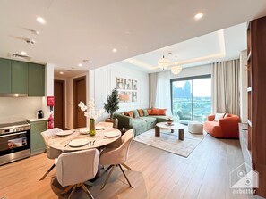 A modern living room with a green sofa, orange armchair, and a dining area with a round table and chairs. - Chic & Cozy 1BR in Heart of City Walk (Dubai)