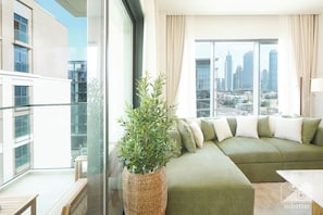 A modern living room with a green sofa, a large window with a city view, and a wicker plant. - Stylish City Walk 2BR Apt Balcony Iconic Views (Dubai)