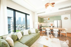 A modern living room with a green sofa, a dining table with chairs, and a kitchen area visible through an open door. - Stylish City Walk 2BR Apt Balcony Iconic Views (Dubai)