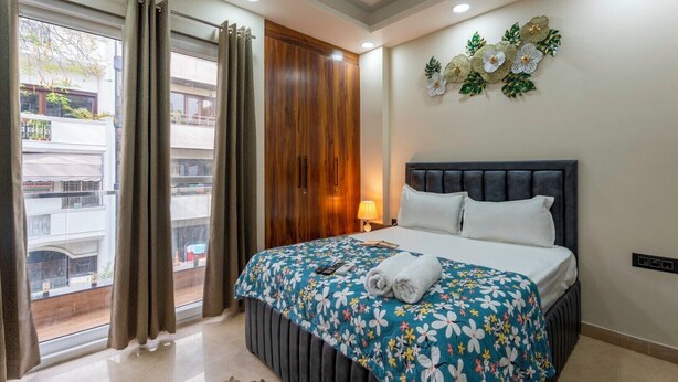Ein Hotelzimmer mit Bett, einem Vorhangfenster, einer Wanddekoration mit Blumen und Blick auf den Balkon.