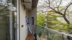 Ein schmaler Balkon mit Holzboden, Glasgeländer und einer blau-weißen Leiter, die an der Wand lehnt.