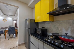 A modern kitchen with a black refrigerator, a stove with a red pot, and yellow cabinets. - Fortune Home Service Apartment 3BHK, J-267 (New Delhi)