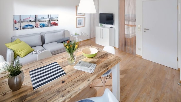 Ett modernt vardagsrum med ett matbord i trä, en grå soffa och en tv som står på ett skåp.