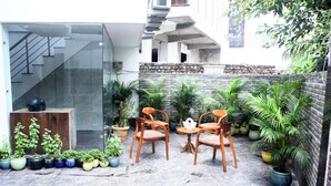 A modern outdoor patio with a stone wall, potted plants, and wooden chairs. - Hotel Fortune Home (Noida)