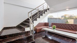 A modern interior with a marble staircase, a brown leather sofa, and a potted plant. - Hotel Fortune Home (Noida)